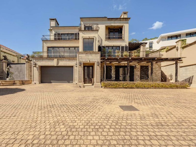 Impressive multi-story residence featuring a paved driveway, double garage, stone facade, and elegant wrought iron balcony detailing.