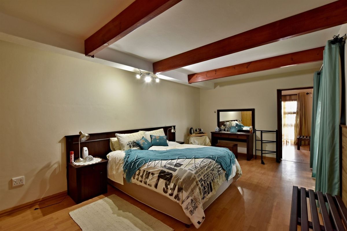 Spacious bedroom featuring exposed timber ceiling beams, laminate flooring, and a built-in headboard with integrated bedside tables.