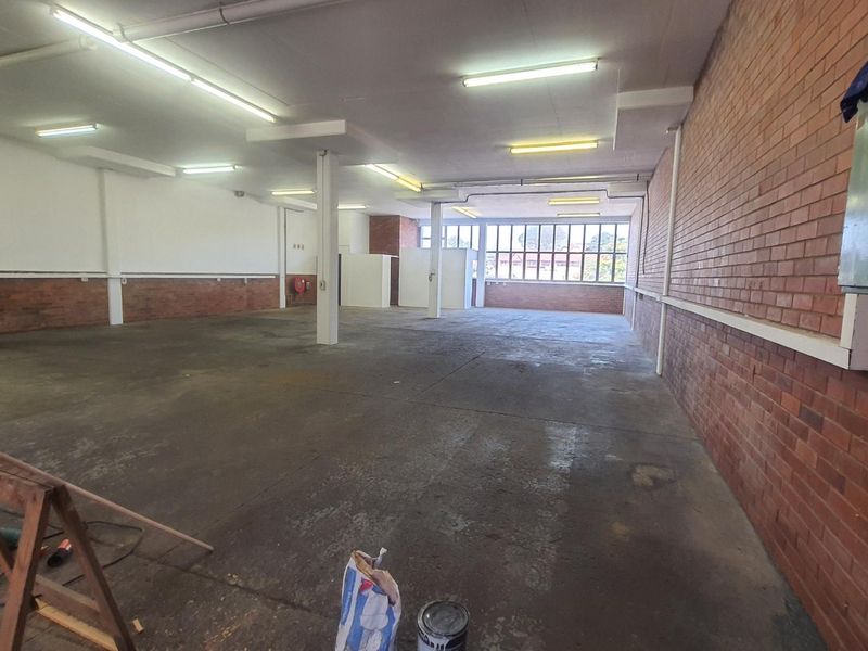 Spacious open-plan industrial unit featuring exposed brick walls, concrete flooring, and ample natural light through large windows, suitable for various commercial or workshop uses.