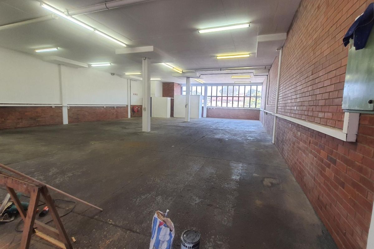 Spacious open-plan industrial unit featuring exposed brick walls, concrete flooring, and ample natural light through large windows, suitable for various commercial or workshop uses.