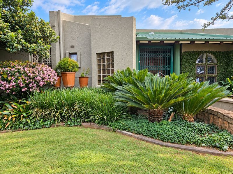 Front facade of the house featuring textured stucco walls, a metal roof, and a landscaped garden with a stone retaining wall.