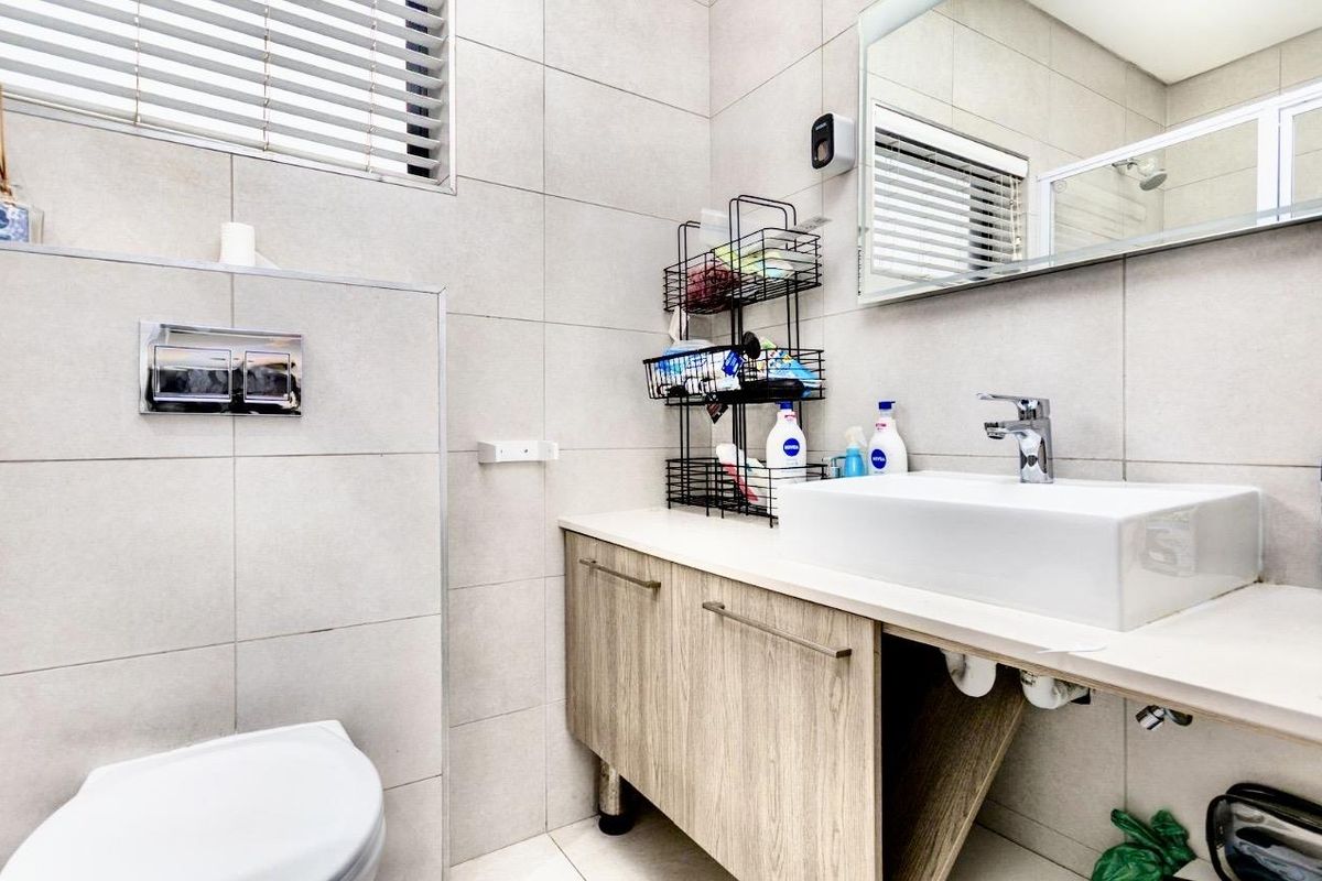 Modern bathroom featuring a wall-mounted toilet, a contemporary vessel sink with a vanity cabinet, and neutral wall tiling.