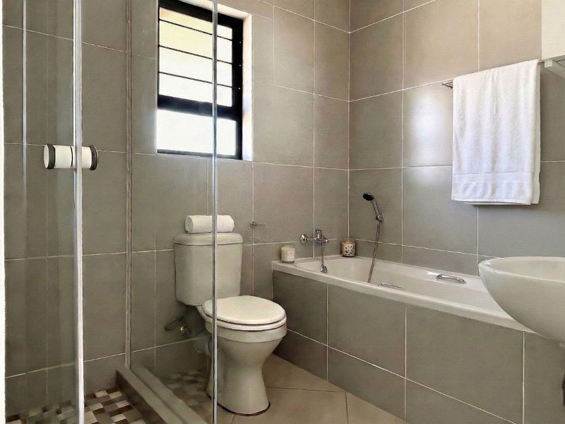 Modern bathroom featuring a glass-enclosed shower, a built-in bathtub, and neutral ceramic wall tiling throughout.