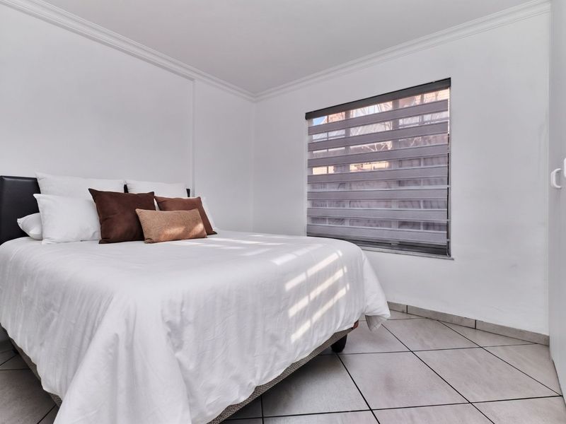 A bright bedroom featuring neutral tiled flooring, built-in wardrobe storage, and modern roller blinds, offering a clean and functional living space.