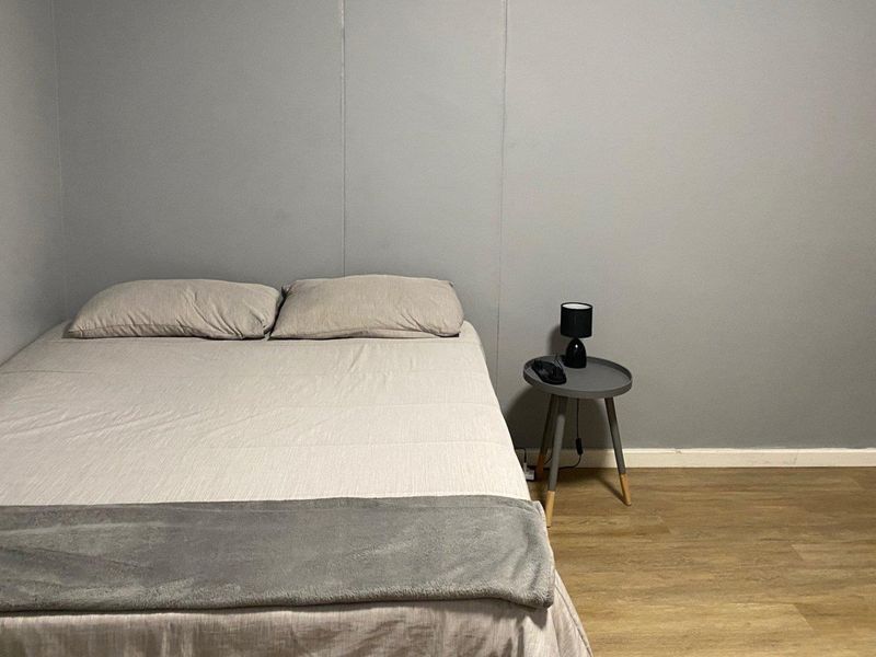 A simple bedroom featuring neutral grey walls and durable laminate flooring, providing a clean and functional sleeping space.