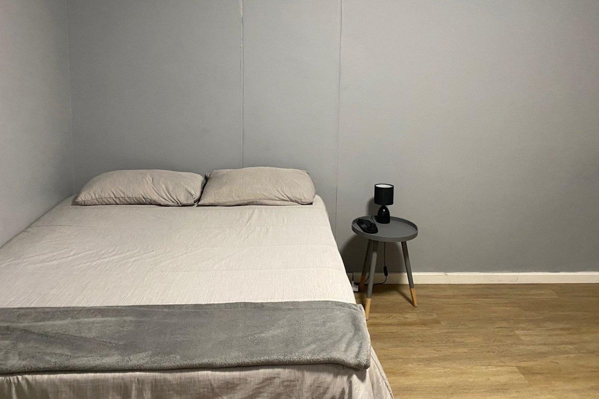 A simple bedroom featuring neutral grey walls and durable laminate flooring, providing a clean and functional sleeping space.