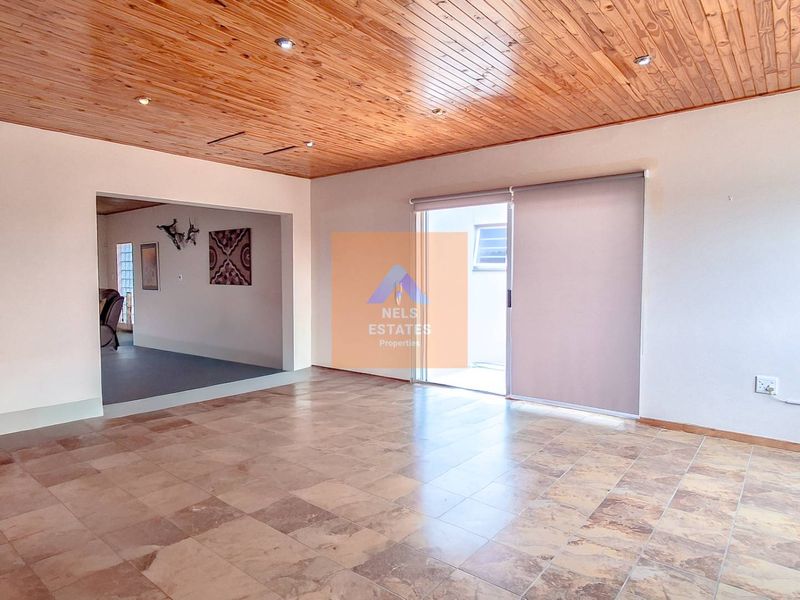 Spacious living area featuring a timber-clad ceiling, tiled flooring, and a sliding glass door providing access to the exterior.