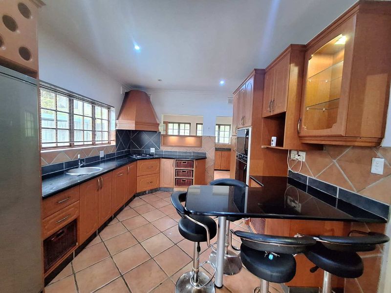 A functional kitchen featuring wooden cabinetry, granite countertops, a built-in oven, gas hob, and tiled flooring with a breakfast nook area.