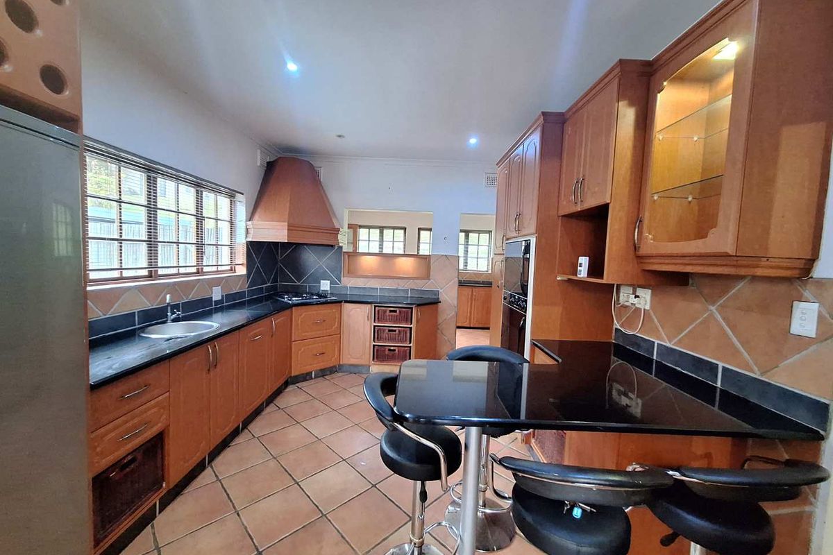 A functional kitchen featuring wooden cabinetry, granite countertops, a built-in oven, gas hob, and tiled flooring with a breakfast nook area.