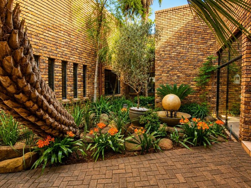 A beautifully landscaped rear courtyard featuring exposed brick walls, paved flooring, and a central stone water feature.