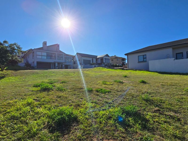 A vacant residential plot of land featuring a gentle slope and established grass, situated within a developed neighborhood setting.