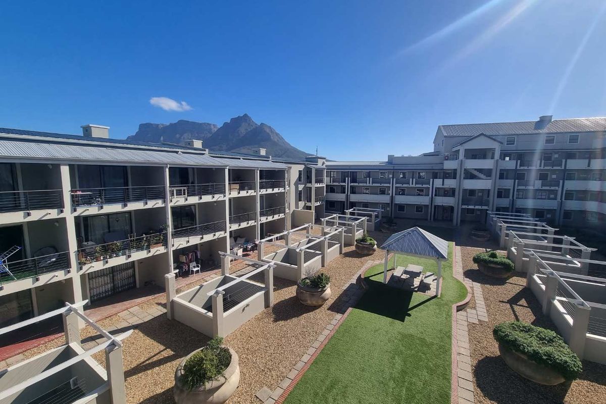 An elevated view of a well-maintained apartment complex courtyard featuring landscaped gravel areas, artificial turf, a covered gazebo, and private balconies.
