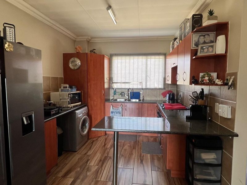 A functional kitchen featuring wood-look floor tiles, granite countertops, ample laminate cabinetry, and a double bowl sink with a tiled backsplash.