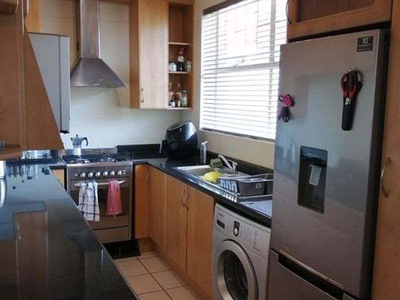 A functional kitchen featuring wooden cabinetry, granite countertops, a stainless steel gas stove with extractor fan, and an integrated washing machine.