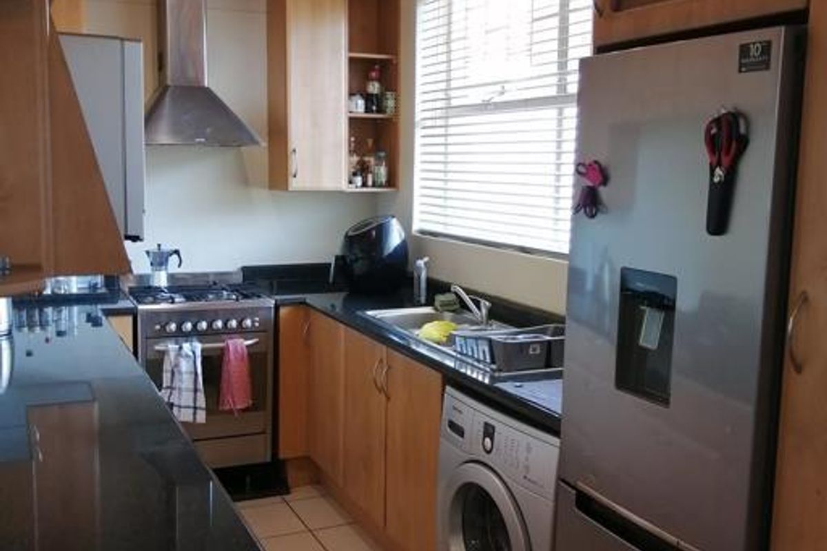 A functional kitchen featuring wooden cabinetry, granite countertops, a stainless steel gas stove with extractor fan, and an integrated washing machine.