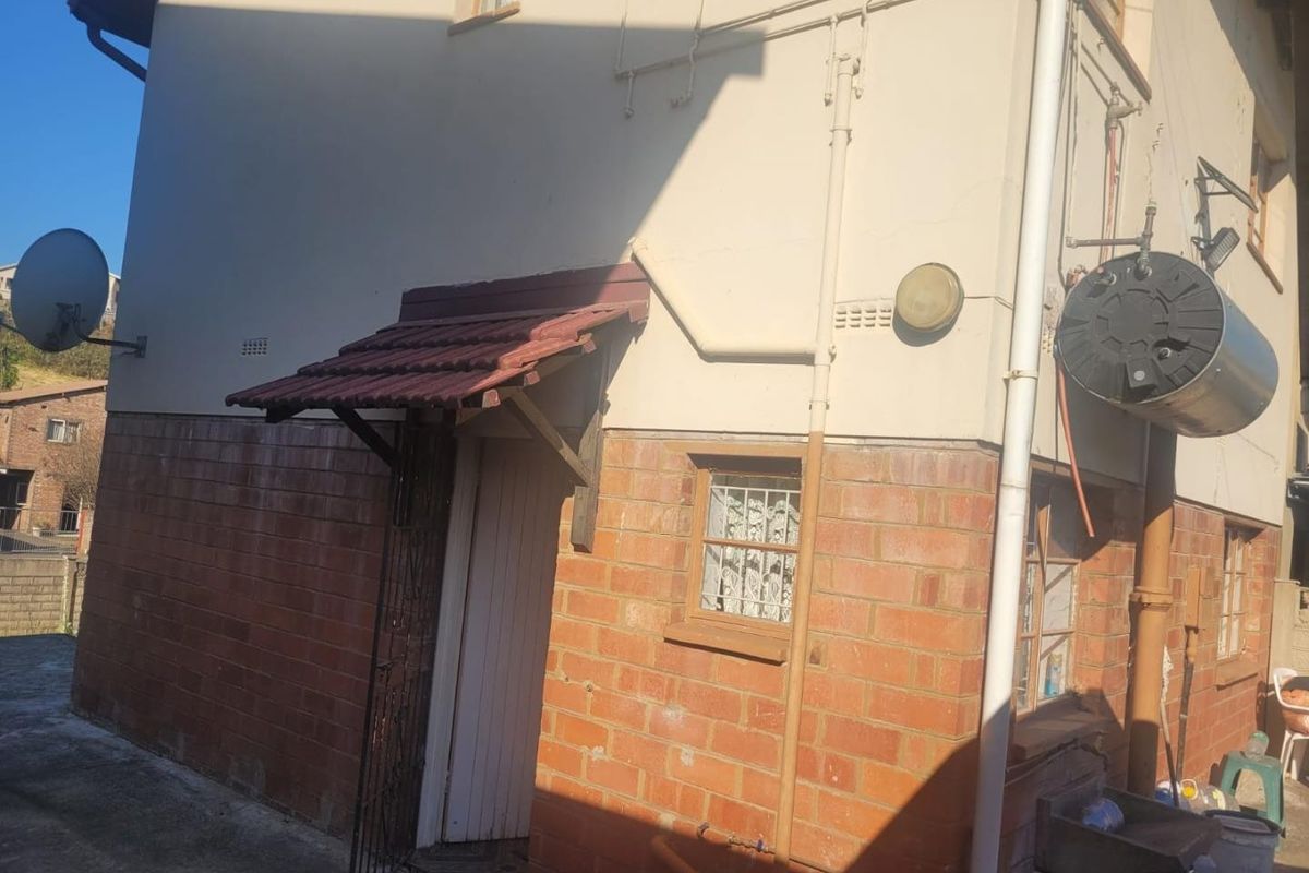 Rear exterior view of the property featuring brick and plaster facade, external geyser, utility sink, and a small tiled entrance awning.