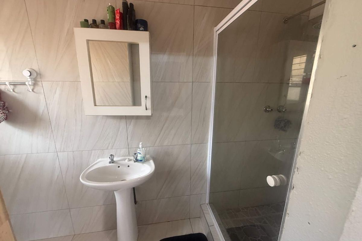 A functional bathroom featuring a pedestal basin, wall-mounted medicine cabinet, and a glass-enclosed shower with neutral wall tiling.