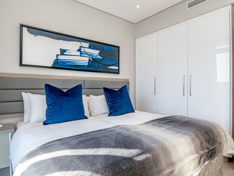 Modern bedroom featuring a sleek built-in wardrobe, upholstered headboard, and recessed ceiling lighting, creating a clean and contemporary living space.