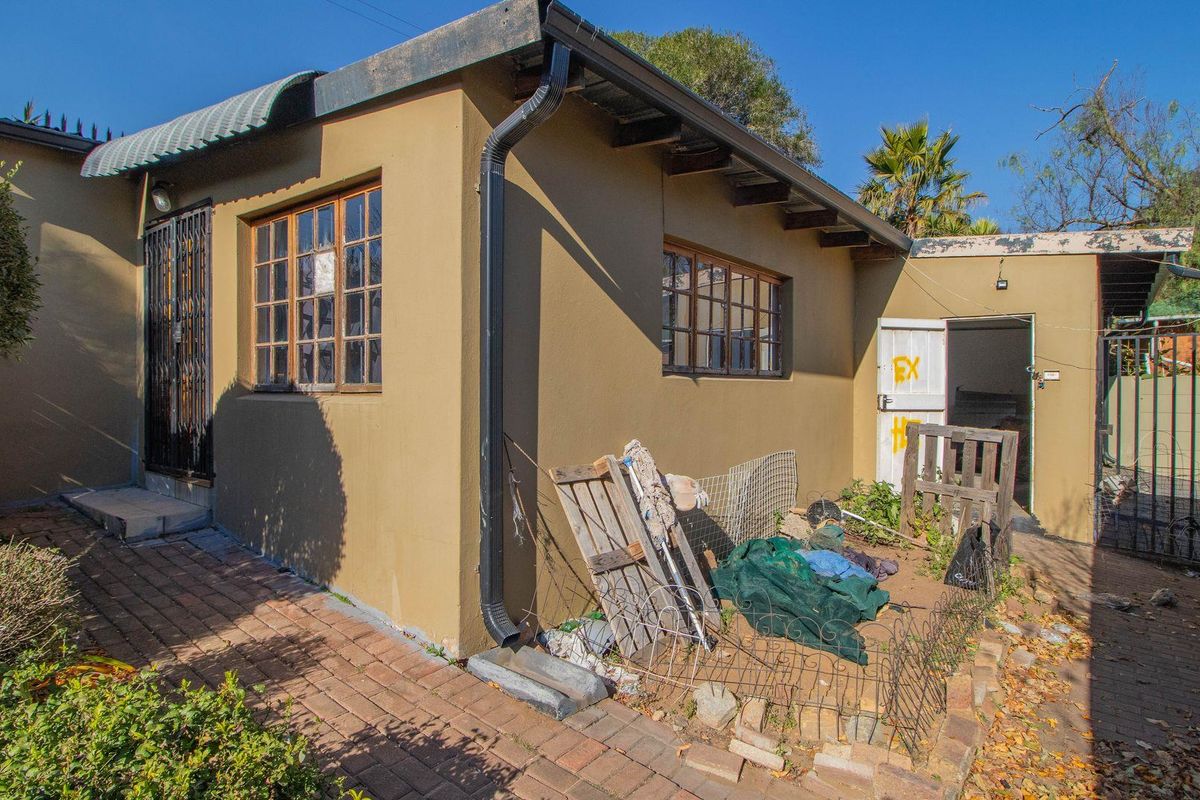 Exterior view of the property showing a side entrance, brick paving, and basic building structure with visible wear on finishes.