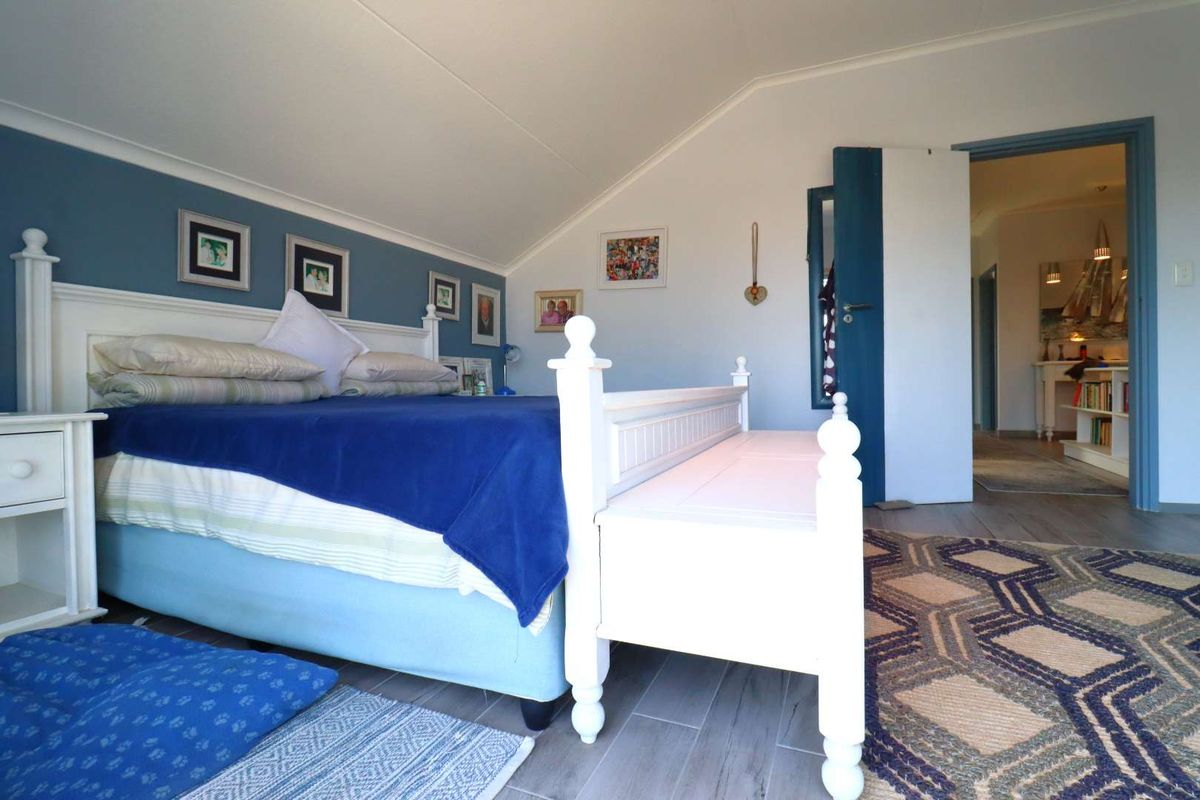 A bedroom featuring a vaulted ceiling, tiled flooring, and a blue accent wall, with an open doorway leading to an adjacent hallway.