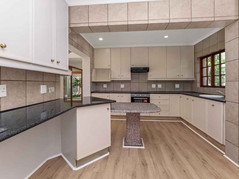 Spacious kitchen featuring neutral cabinetry, granite countertops, integrated oven, extractor fan, and modern laminate flooring, offering a clean and functional workspace.