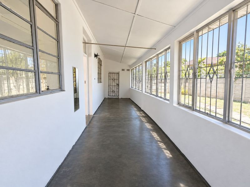 A bright, enclosed sunroom or patio featuring concrete flooring, extensive steel-framed windows with security bars, and a secure access door.