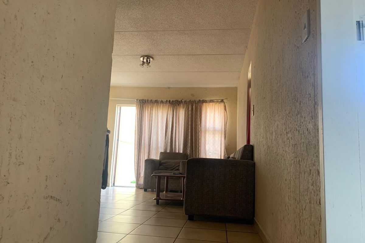A living room area featuring tiled flooring and a sliding glass door leading to an outdoor space, with dated wall finishes and ceiling tiles.