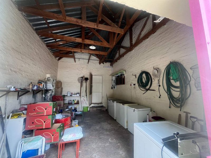 A functional utility or storage space featuring exposed timber roof trusses, painted brick walls, and concrete flooring, suitable for workshop or storage use.