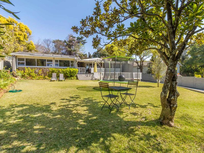 Spacious rear garden featuring a well-maintained lawn, mature trees, and a raised timber deck with access to the main house via sliding glass doors.