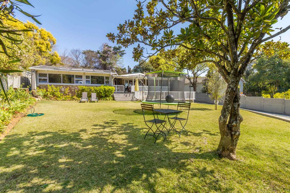 Spacious rear garden featuring a well-maintained lawn, mature trees, and a raised timber deck with access to the main house via sliding glass doors.