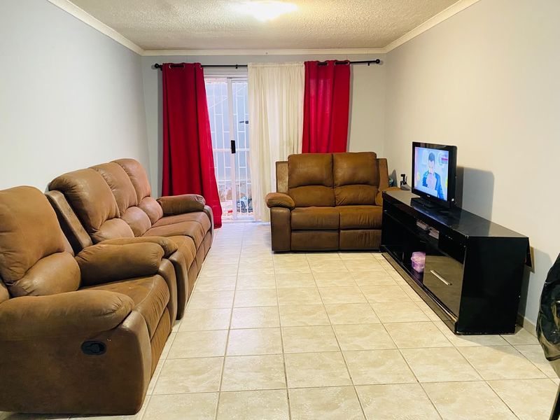 A functional living room featuring tiled flooring and a sliding glass door with security gate, providing access to the exterior.