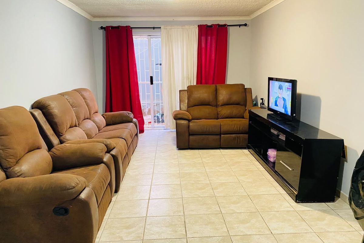 A functional living room featuring tiled flooring and a sliding glass door with security gate, providing access to the exterior.
