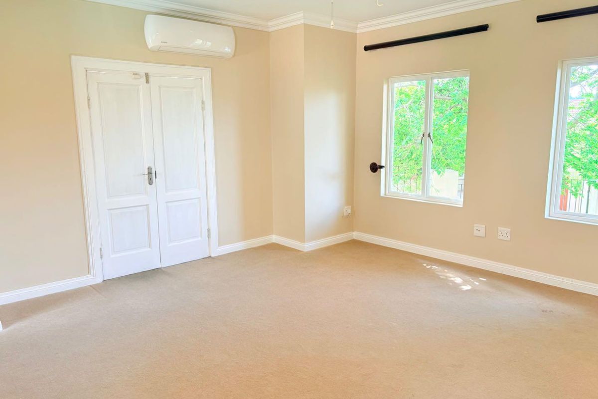 A spacious, empty bedroom featuring neutral carpet flooring, crown molding, double doors, and a wall-mounted split-system air conditioner.