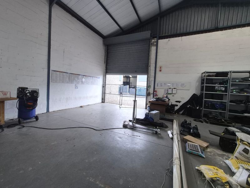 Industrial utility space featuring high ceilings with exposed steel trusses, concrete flooring, and a large roller shutter door for easy access.