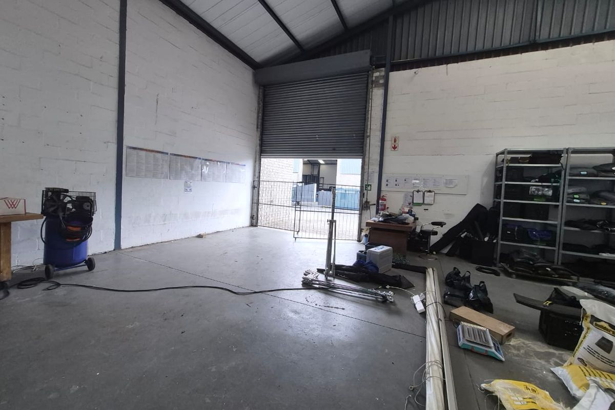 Industrial utility space featuring high ceilings with exposed steel trusses, concrete flooring, and a large roller shutter door for easy access.
