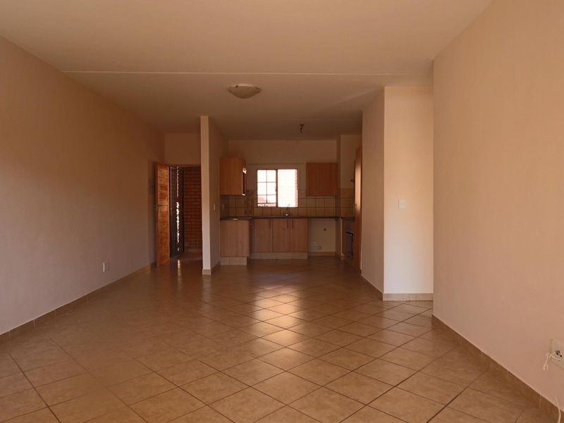 An open-plan living and kitchen area featuring neutral walls, tiled flooring, and functional built-in kitchen cabinetry.