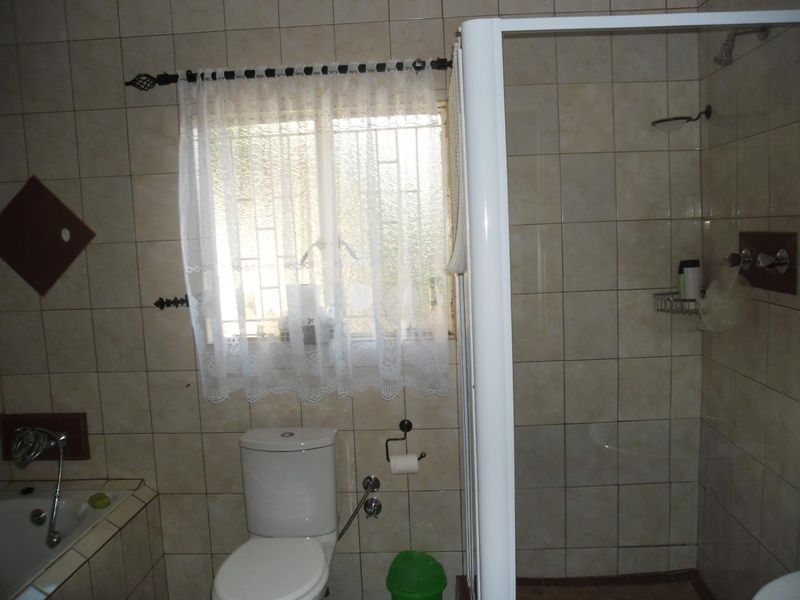 A functional bathroom featuring a built-in bathtub, separate shower enclosure, and toilet, finished with neutral wall tiling and security bars on the window.