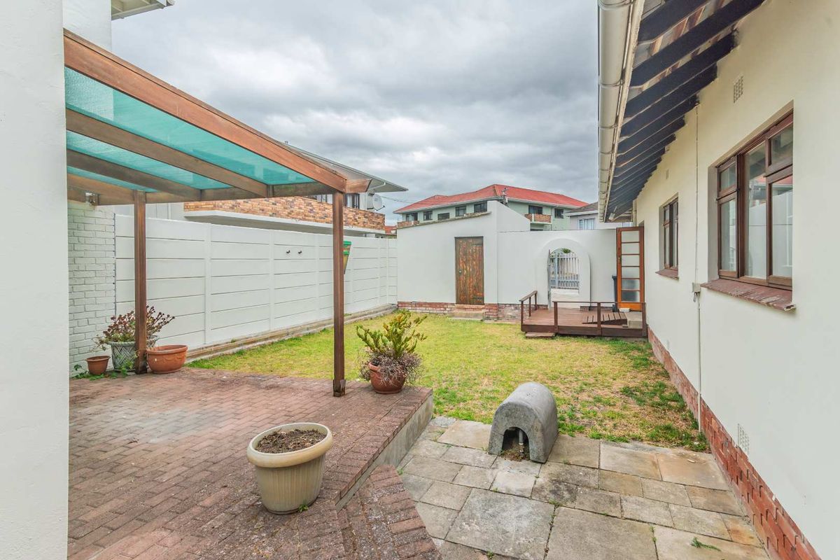 A private rear garden featuring a paved patio area, a timber pergola, and a small lawn with perimeter walling.