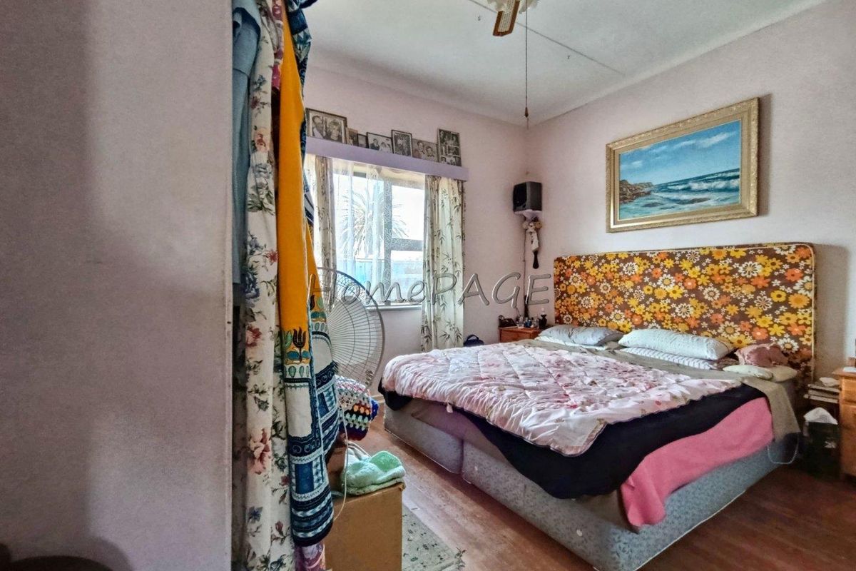 A bedroom featuring a ceiling fan, large window, and laminate flooring. The space requires cosmetic updates to modernize the interior finishes.