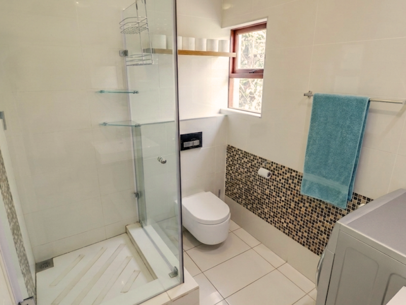 Modern bathroom featuring a glass-enclosed shower, wall-mounted toilet, and stylish mosaic tile accents, providing a clean and functional space.