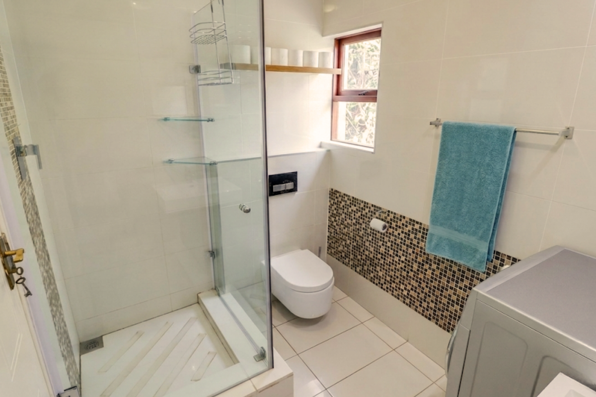 Modern bathroom featuring a glass-enclosed shower, wall-mounted toilet, and stylish mosaic tile accents, providing a clean and functional space.