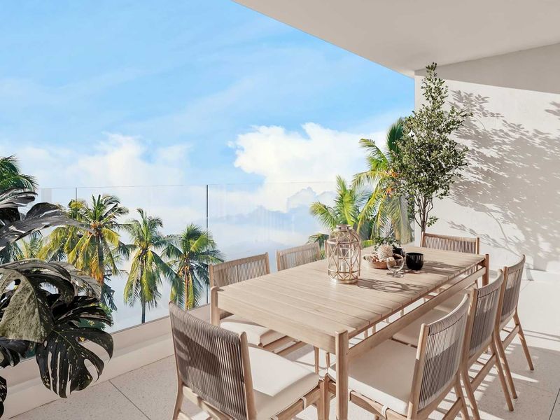 A spacious, modern covered balcony featuring a sleek glass balustrade and tiled flooring, offering an open-air setting with scenic tropical views.