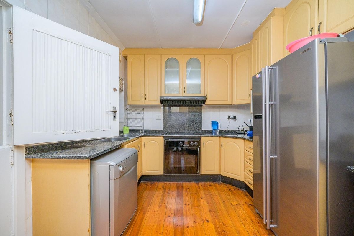 A functional kitchen featuring warm-toned built-in cabinetry, granite countertops, integrated oven, extractor fan, and polished hardwood flooring.