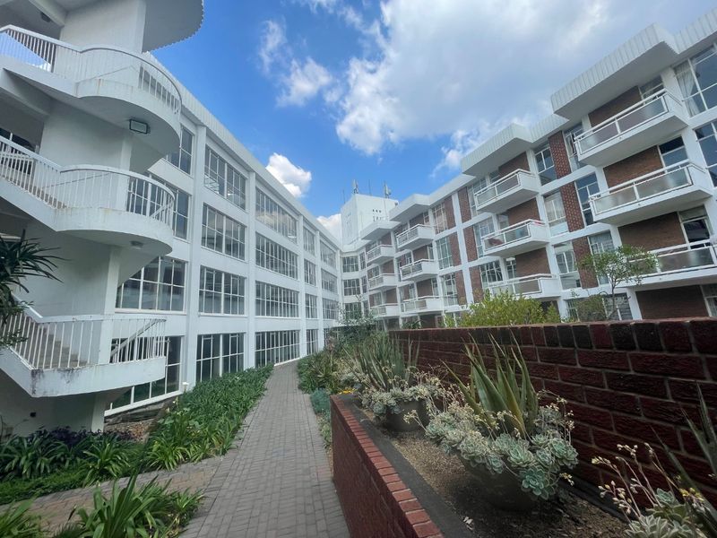 Exterior view of the apartment complex featuring multi-level balconies, brick facade detailing, and a landscaped paved walkway between building wings.