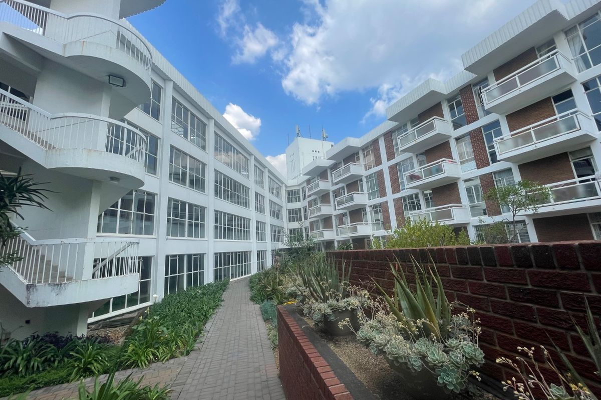 Exterior view of the apartment complex featuring multi-level balconies, brick facade detailing, and a landscaped paved walkway between building wings.