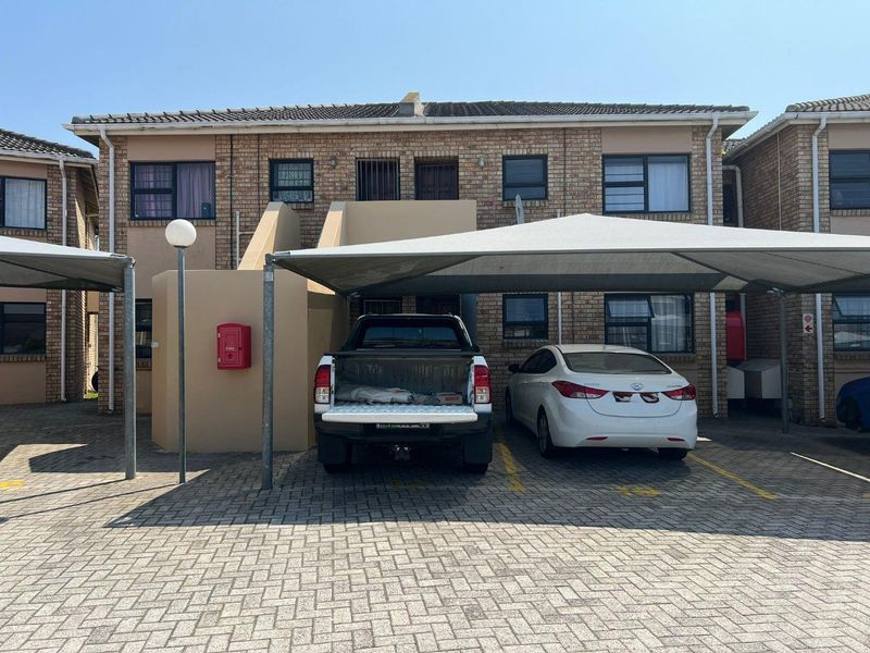 Front elevation of a multi-story apartment complex featuring brick facade, paved parking area, and shade cloth carports.