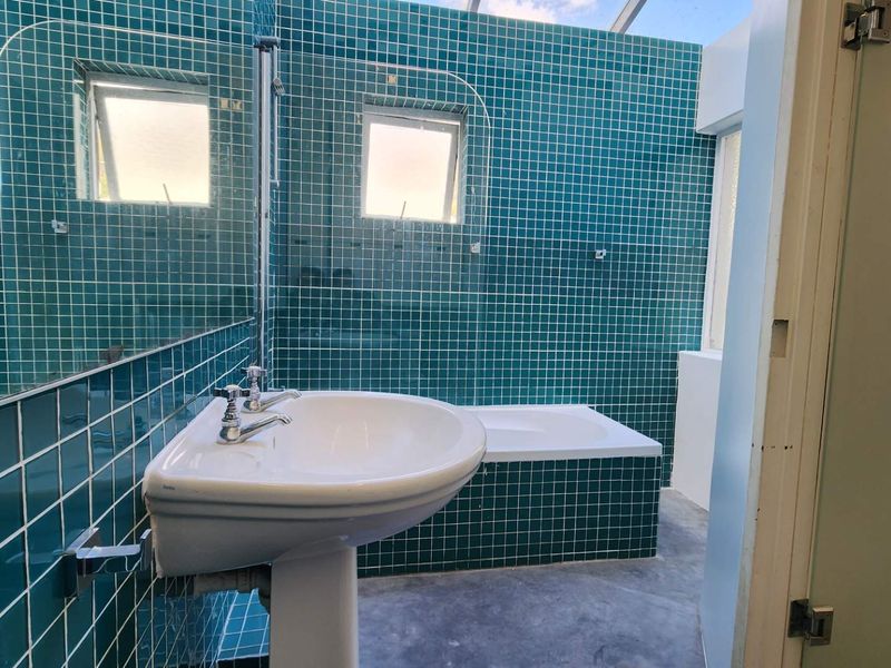 A bathroom featuring teal mosaic wall tiles, a pedestal basin, and a built-in bathtub with a glass screen.