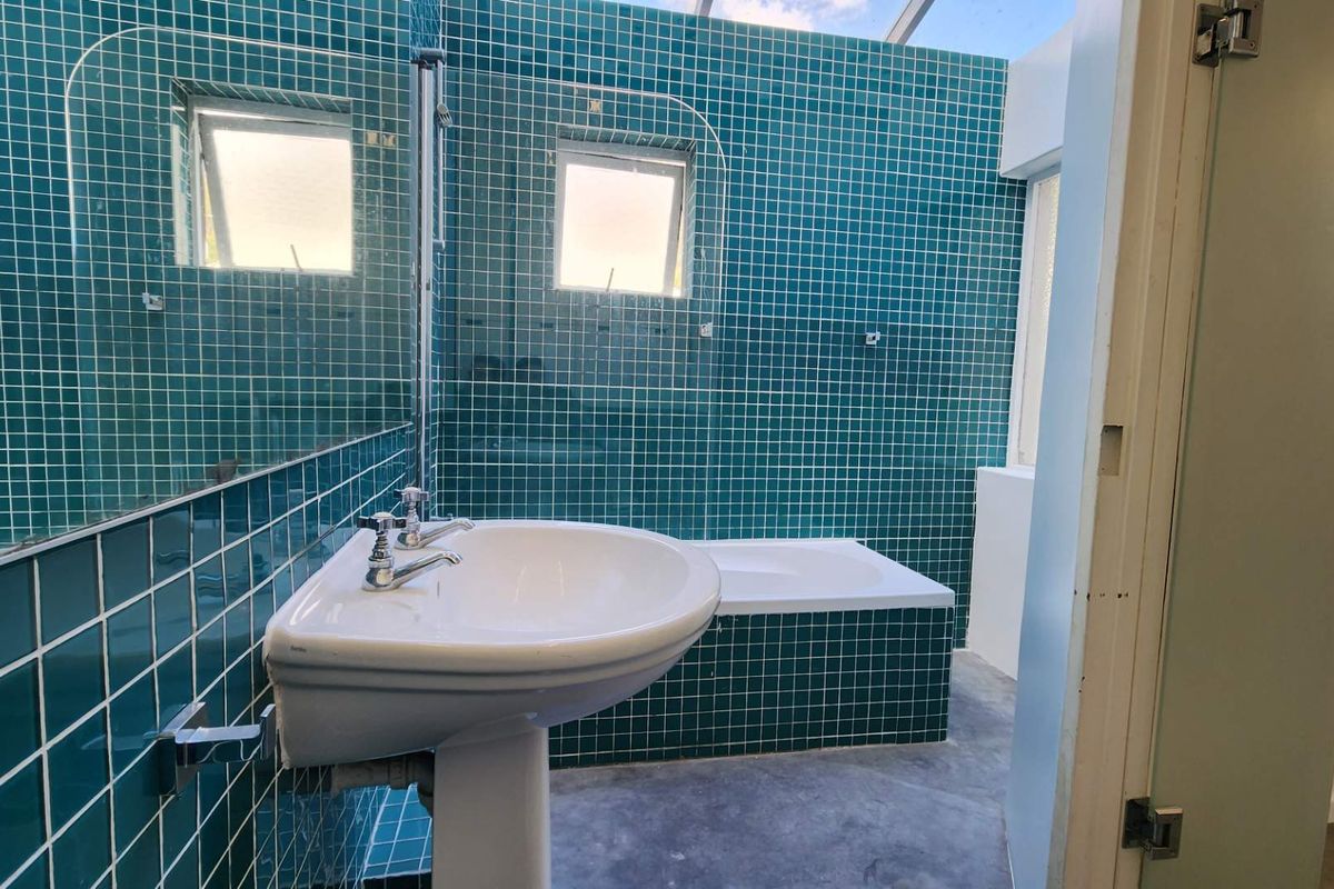 A bathroom featuring teal mosaic wall tiles, a pedestal basin, and a built-in bathtub with a glass screen.