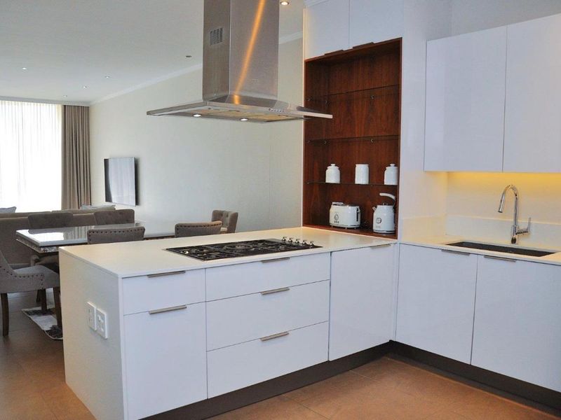 Modern open-plan kitchen featuring sleek white cabinetry, stone countertops, integrated gas cooktop, and stainless steel extractor fan, seamlessly flowing into the living area.