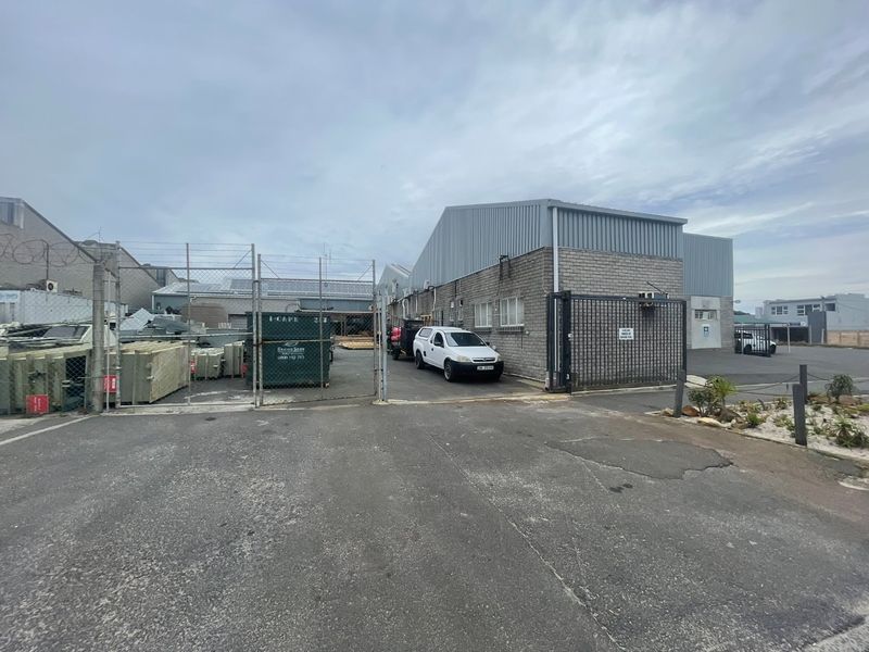 Industrial property exterior featuring a brick and metal facade, secure gated entrance, and paved driveway area.
